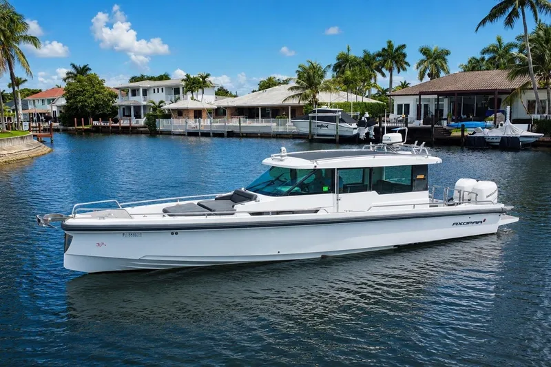 The Image of 2018 Axopar 37 Sports Cabin boat on a sunny waterfront with palm trees. - 0