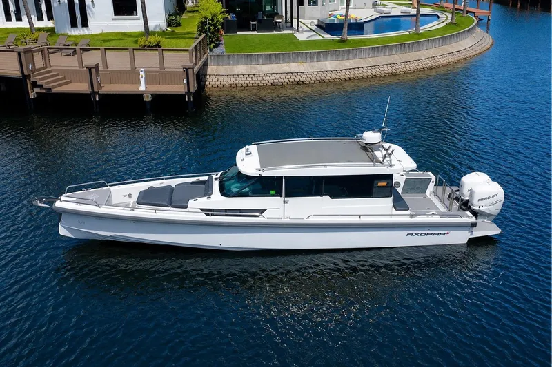 Slide: The Image of 2018 Axopar 37 Sports Cabin boat on calm water near a modern waterfront property. - 1