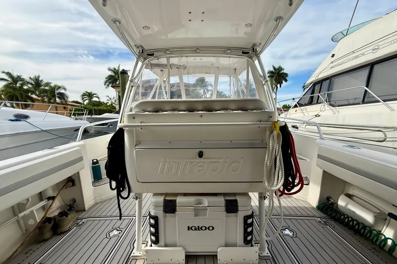 Slide: The Image of 2003 Intrepid 348 Walkaround boat interior with seating and storage, docked near palm trees. - 5