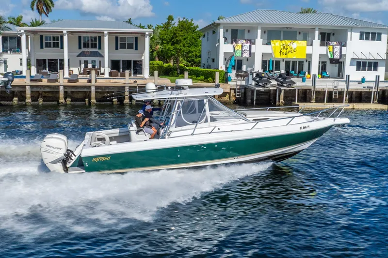 Slide: The Image of 2003 Intrepid 348 Walkaround boat cruising near waterfront homes, featuring Mercury engines. - 12