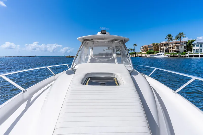 Slide: The Image of 2003 Intrepid 348 Walkaround boat cruising near luxury waterfront homes under a clear blue sky. - 23