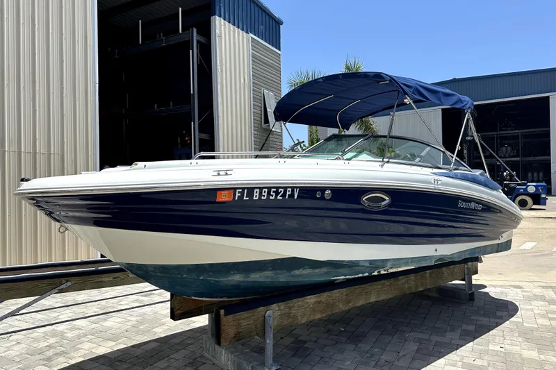 Slide: The Image of 2014 SouthWind 2400 SD boat with blue canopy, docked outside a warehouse. - 1