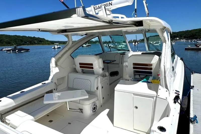 Slide: The Image of 2024 Pursuit DC 326 Dual Console boat docked on a serene lake with clear skies. - 8