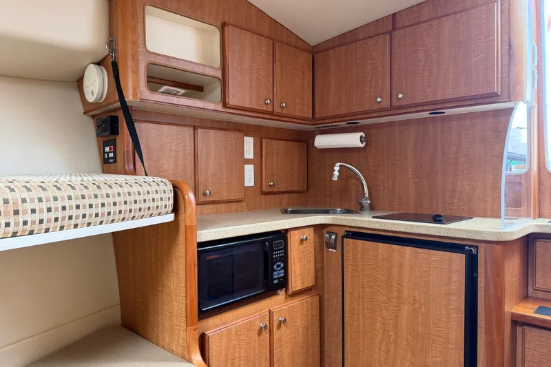 Slide: The Image of 2007 Luhrs 31 Open boat interior with kitchenette, featuring wood cabinets, sink, and microwave. - 14