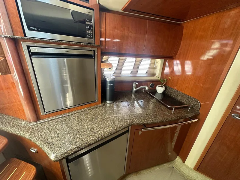 Slide: The Image of The 2006 Sea Ray 380 Sundancer's galley features a sleek countertop, stainless steel appliances, and wood paneling. - 5