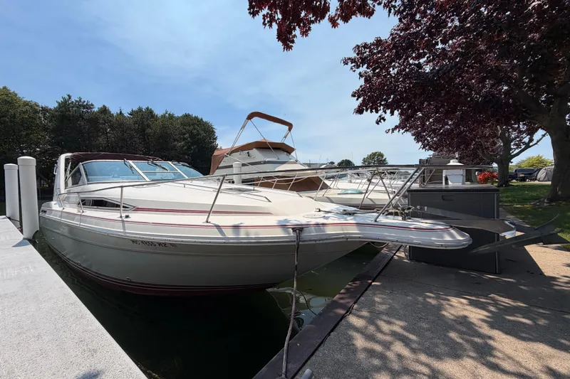 The Image of 1989 Sea Ray Sundancer 280 docked at marina, surrounded by trees and clear sky. - 1