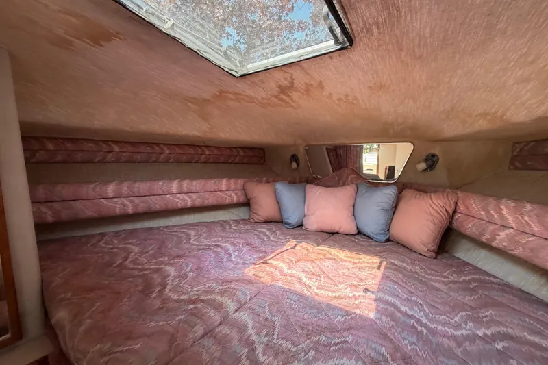 Slide: The Image of 1989 Sea Ray Sundancer 280 cabin interior with cozy bedding and pillows under a skylight. - 28