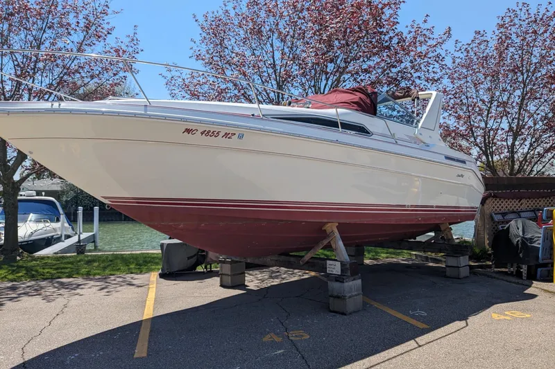 Slide: The Image of 1990 Sea Ray Sundancer 280 boat on stands, surrounded by trees and parked in a marina. - 44