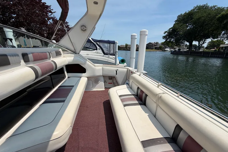 Slide: The Image of 1989 Sea Ray Sundancer 280 boat interior with cushioned seating, docked by a scenic waterfront. - 14