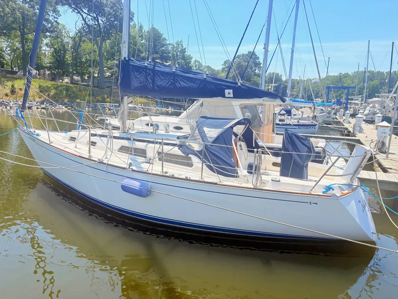 The Image of A white sailboat docked in a calm marina, featuring blue covers and ropes. - 0