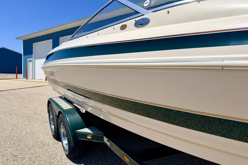 Slide: The Image of 2002 Larson LXi 210 boat on trailer, parked near blue building under clear sky. - 7