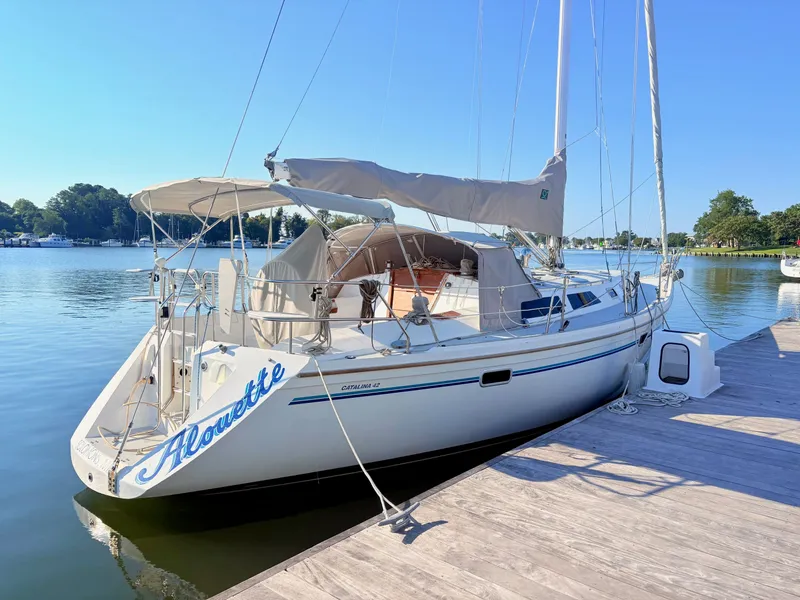 The Image of A white 1994 Catalina 42 sailboat docked at a calm pier, featuring a beige sail cover. - 0
