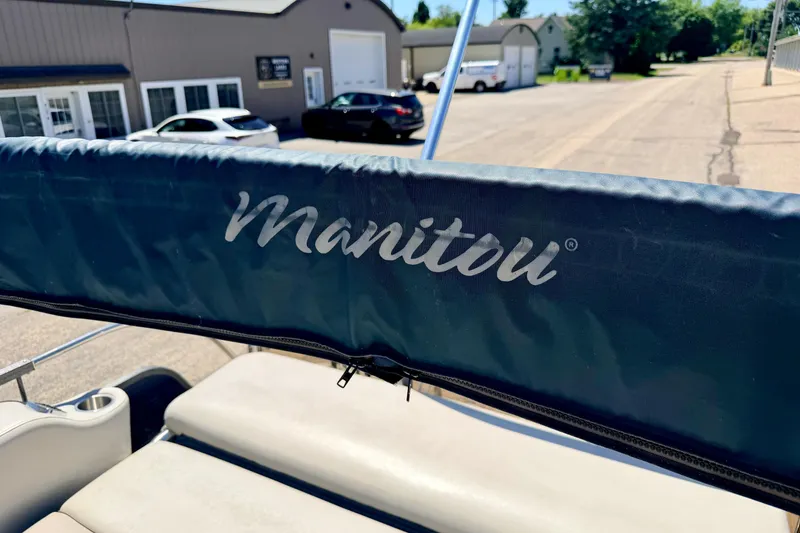 Slide: The Image of 2015 Manitou 25 SES BENCH boat with logo, parked near buildings. - 68