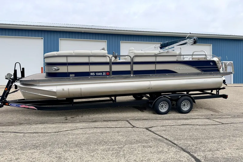 Slide: The Image of 2015 Manitou 25 SES BENCH pontoon boat on trailer, parked outside blue building. - 3