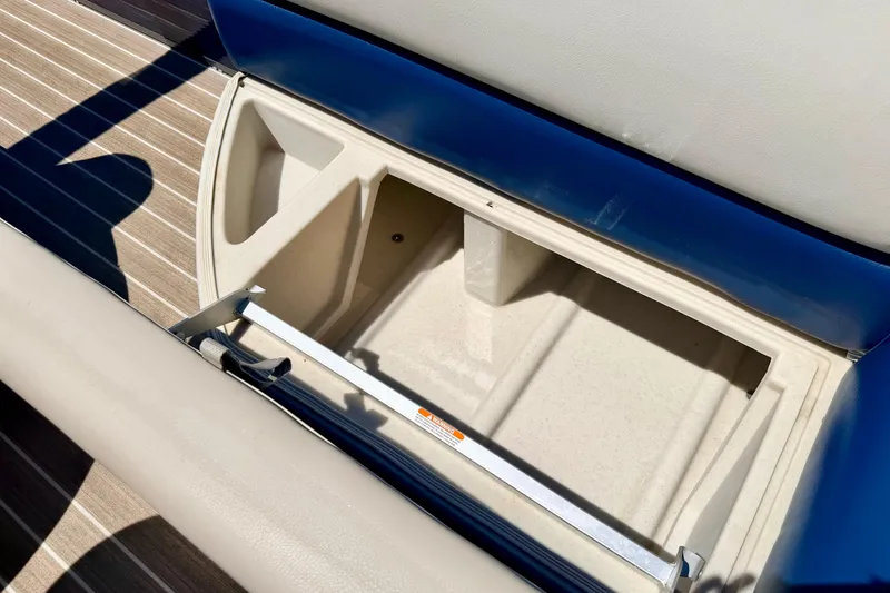 Slide: The Image of Open storage compartment on 2015 Manitou 25 SES BENCH boat, featuring beige interior and blue seating. - 66