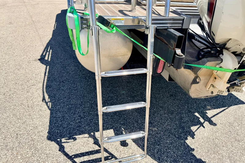 Slide: The Image of 2015 Manitou 25 SES BENCH boat ladder and motor detail on asphalt surface. - 23