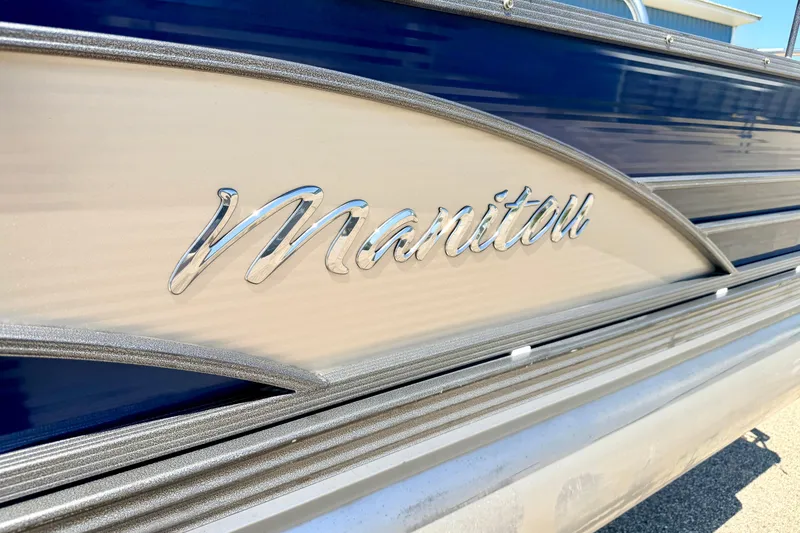 Slide: The Image of 2015 Manitou 25 SES BENCH boat with chrome logo detail. - 14