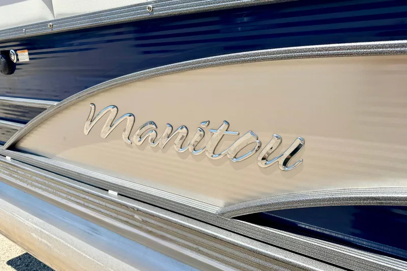 Slide: The Image of 2015 Manitou 25 SES BENCH boat with sleek metallic logo detail. - 7