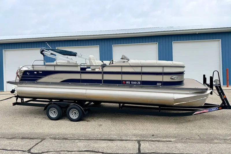 Slide: The Image of 2015 Manitou 25 SES BENCH pontoon boat on trailer, parked by blue garage. - 4