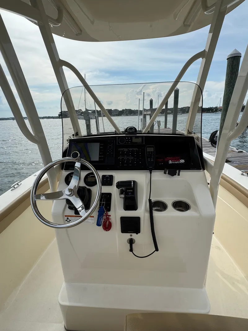 Slide: The Image of The image shows the helm of a 2019 Scout 215 XSF boat. It features a modern design with a steering wheel, instruments, and cup holders. Water and a dock are visible in the background. - 14