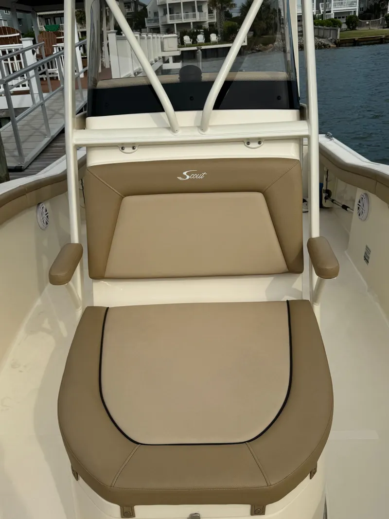 Slide: The Image of A 2019 Scout 215 XSF boat with beige upholstery and armrests, docked by the water. - 26