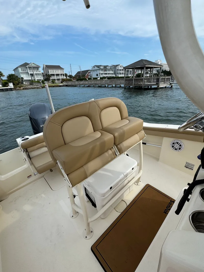 Slide: The Image of The image shows the cockpit of a 2019 Scout 215 XSF boat. It features beige upholstery and is on the water with houses in the background. - 22