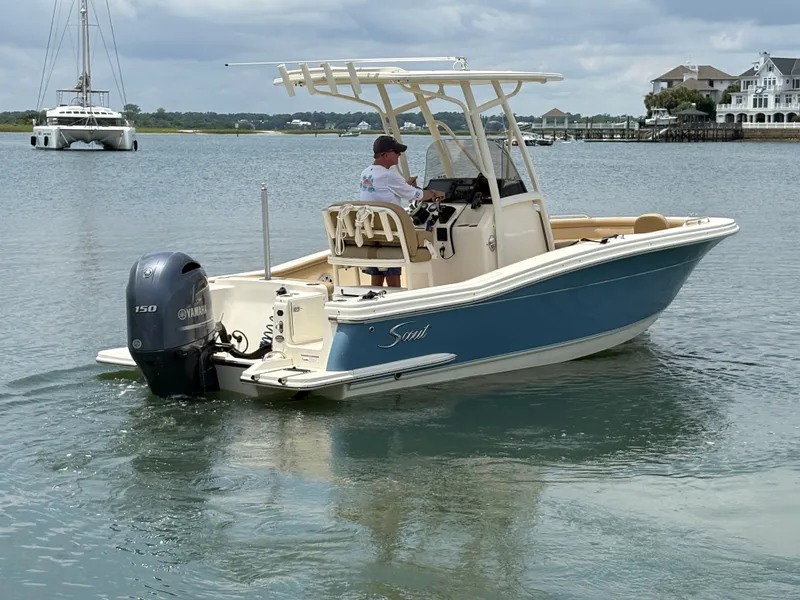 Slide: The Image of A 2019 Scout 215 XSF boat on calm water. It features an outboard motor and a T-top. - 7