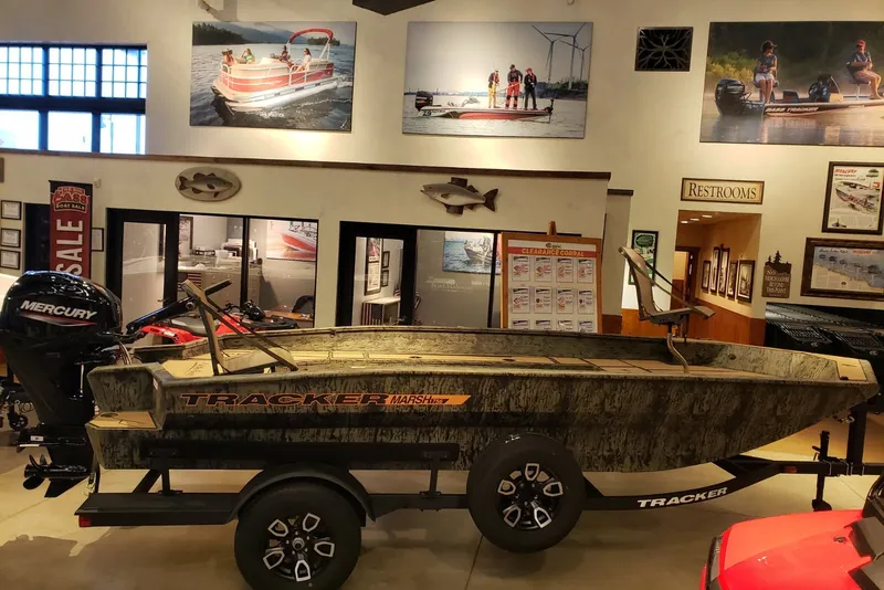 Slide: The Image of 2026 Tracker Grizzly 1756 T Marsh boat displayed in showroom with Mercury engine. - 2