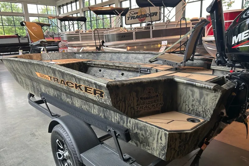 Slide: The Image of 2026 Tracker Grizzly 1756 T Marsh boat in showroom, featuring camouflage design and Mercury engine. - 2