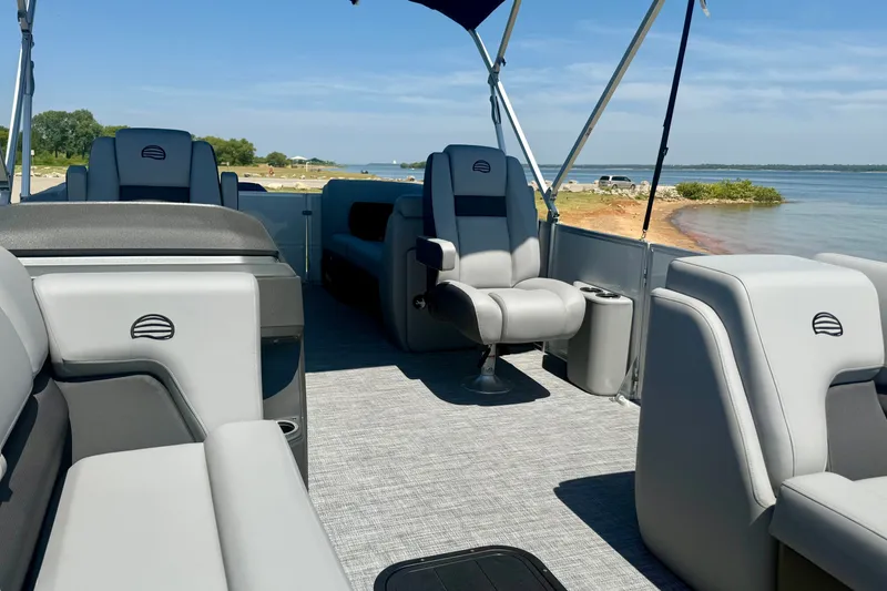 Slide: The Image of 2026 Sun Tracker Party Barge 24 XP3 interior with gray seating, near a scenic lakeside. - 8