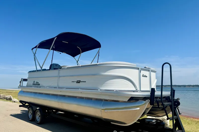 The Image of 2026 Sun Tracker Party Barge 24 XP3 pontoon boat on trailer by a lake. - 0