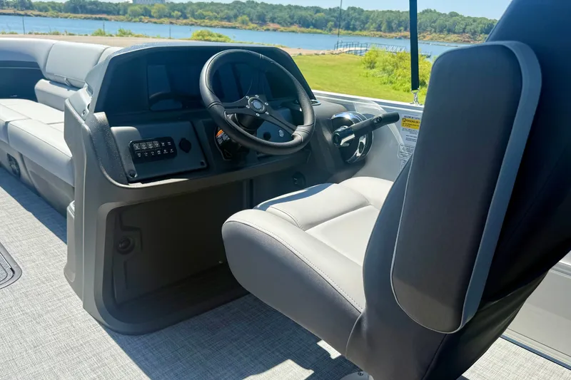 Slide: The Image of 2026 Sun Tracker Party Barge 24 XP3 interior with steering wheel and seating, near a scenic lake. - 6