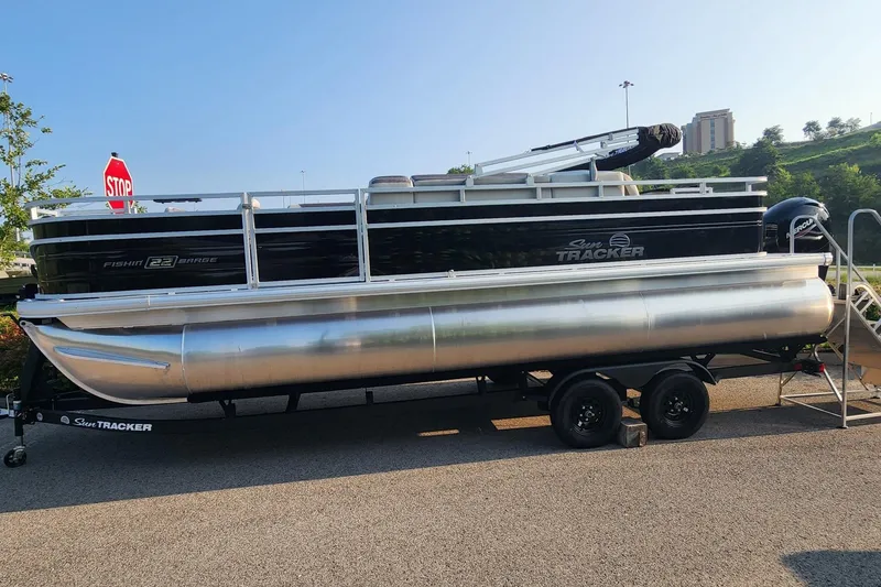 The Image of 2026 Sun Tracker Fishin' Barge 22 XP3 pontoon boat on trailer, parked outdoors. - 1