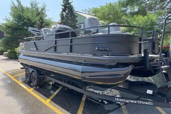 Slide: The Image of 2026 Ranger 220F pontoon boat on trailer, parked outdoors, surrounded by trees. - 1