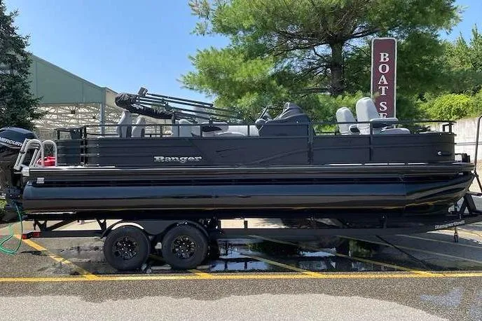 The Image of 2026 Ranger 220F pontoon boat on trailer, parked outdoors near boat sales sign. - 0