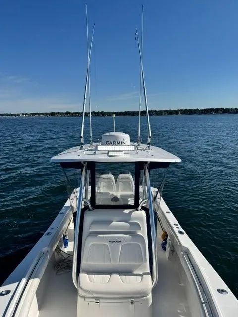 Slide: The Image of A 2015 Regulator 25 boat on calm water. It features a T-top with fishing rod holders. - 14
