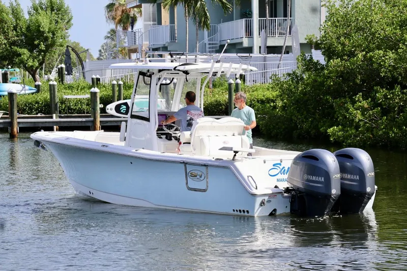 The Image of 2018 Sea Hunt Gamefish 27 Coffin Box boat with dual Yamaha engines on a calm waterway. - 2