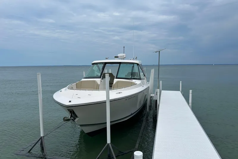 The Image of 2018 Pursuit DC 325 Dual Console boat docked on calm water under cloudy sky. - 0