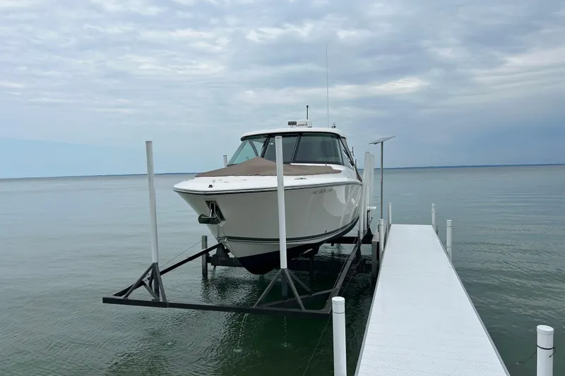 Slide: The Image of 2018 Pursuit DC 325 Dual Console boat on lift by dock, calm water background. - 21