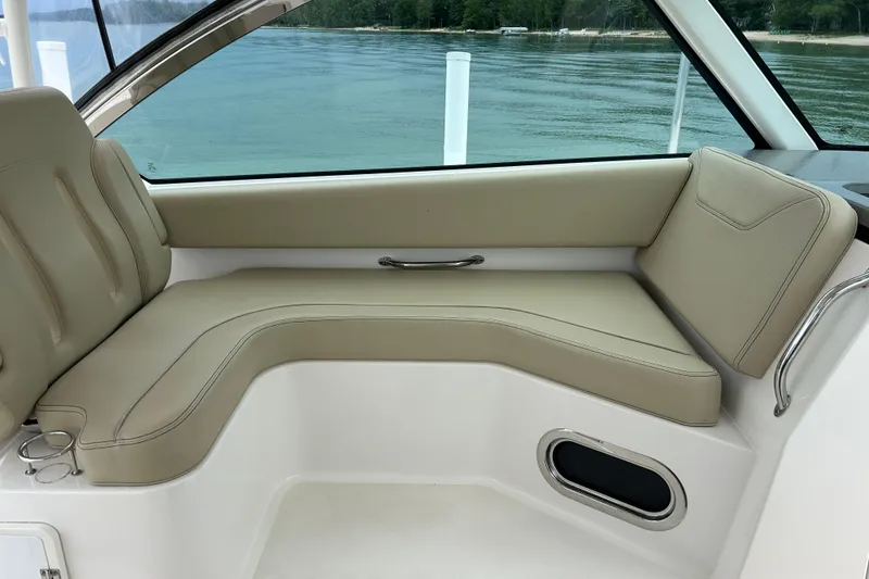 Slide: The Image of 2018 Pursuit DC 325 Dual Console interior with beige seating, overlooking calm waters. - 10
