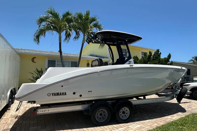 The Image of 2024 Yamaha Boats 255 FSH Sport H on trailer, parked in driveway under clear blue sky. - 1