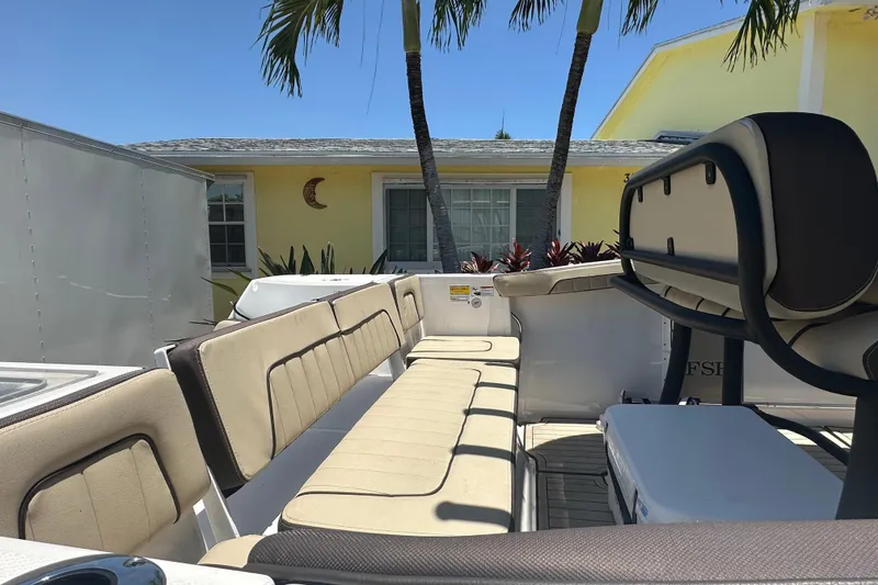 Slide: The Image of 2024 Yamaha Boats 255 FSH Sport H interior with beige seating, parked near a yellow house. - 5