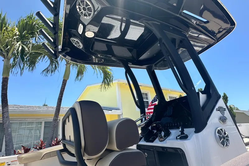 Slide: The Image of 2024 Yamaha Boats 255 FSH Sport H helm with T-top, palm trees, and house in background. - 4