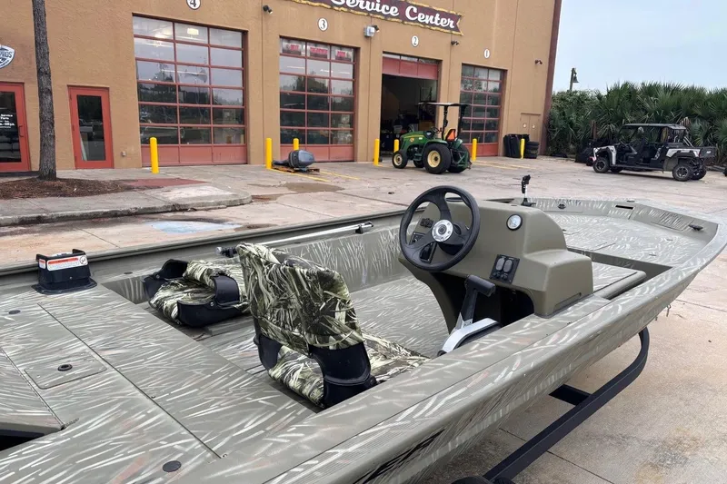 Slide: The Image of 2014 Tracker Grizzly 1754 SC boat at service center, camo seats, outdoor setting. - 4