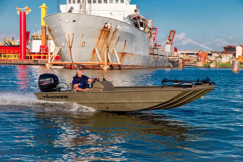 Slide: The Image of A 2024 Tracker Grizzly 1754 SC boat cruising on water in front of a large cargo ship. - 12