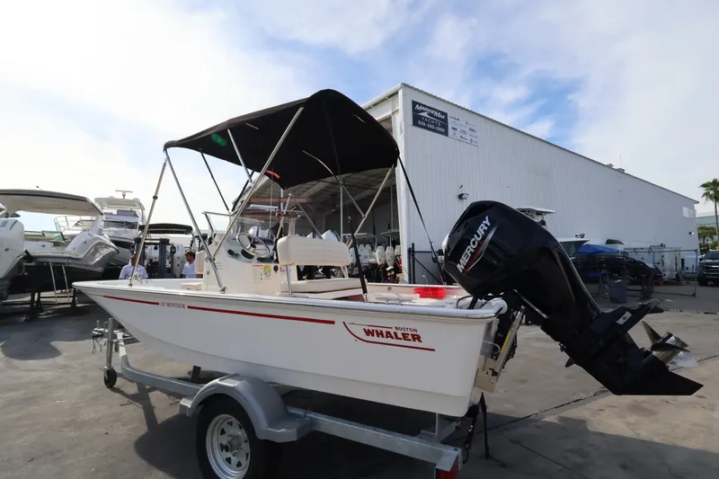 Slide: The Image of A 2027 Boston Whaler 150 Montauk on a trailer. It features a black canopy and a Mercury engine. - 3
