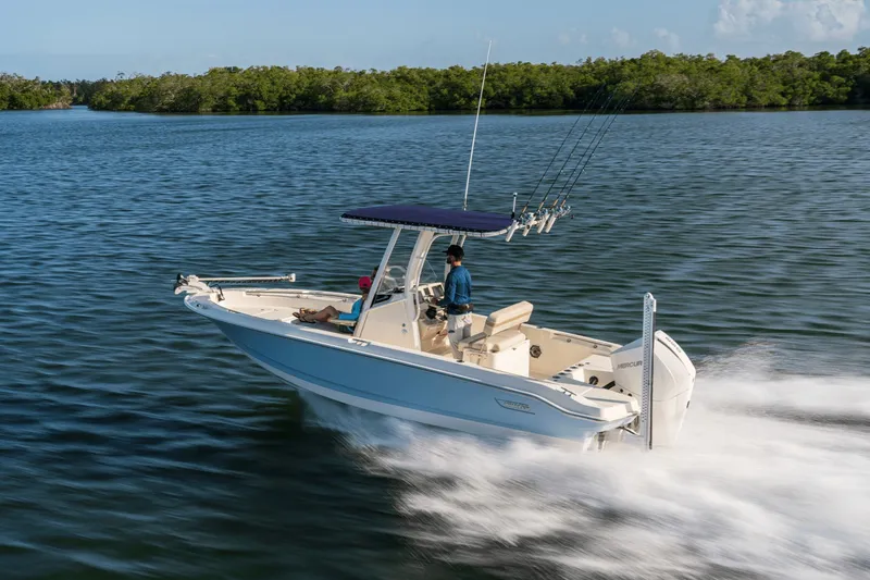 Slide: The Image of A 2027 Boston Whaler 220 Dauntless speeds across calm water, surrounded by lush greenery. - 2