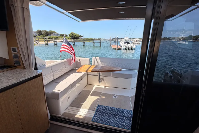 Slide: The Image of 2017 Sea Ray Sundancer 460 yacht interior with seating, table, and American flag by the water. - 12