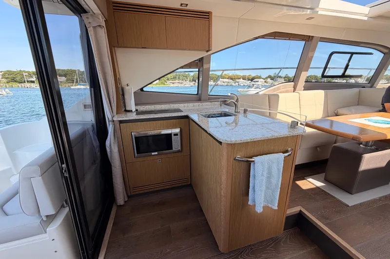 Slide: The Image of 2017 Sea Ray Sundancer 460 yacht interior with kitchenette and seating area, overlooking marina. - 17