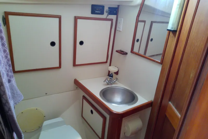 Slide: The Image of Compact bathroom in a 1988 Brewer 44 boat, featuring a sink, mirror, and storage cabinets. - 70